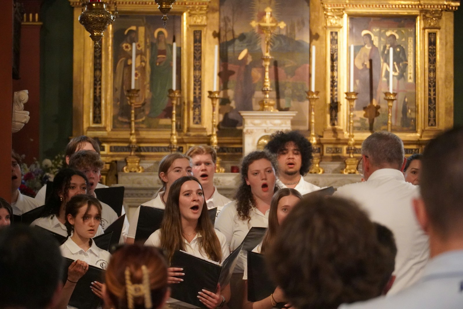 A group of people singing in front of a golden alter